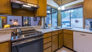 A modern kitchen with wooden cabinets, stainless steel appliances, and a large window providing a view of the outdoors. - Cozy Pet Friendly Cabin, Wood Fireplace, Hot Tub, SHARC passes, close to Village (Sunriver)