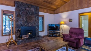 A cozy living room with a stone fireplace, a television, and comfortable seating. - Cozy Pet Friendly Cabin, Wood Fireplace, Hot Tub, SHARC passes, close to Village (Sunriver)
