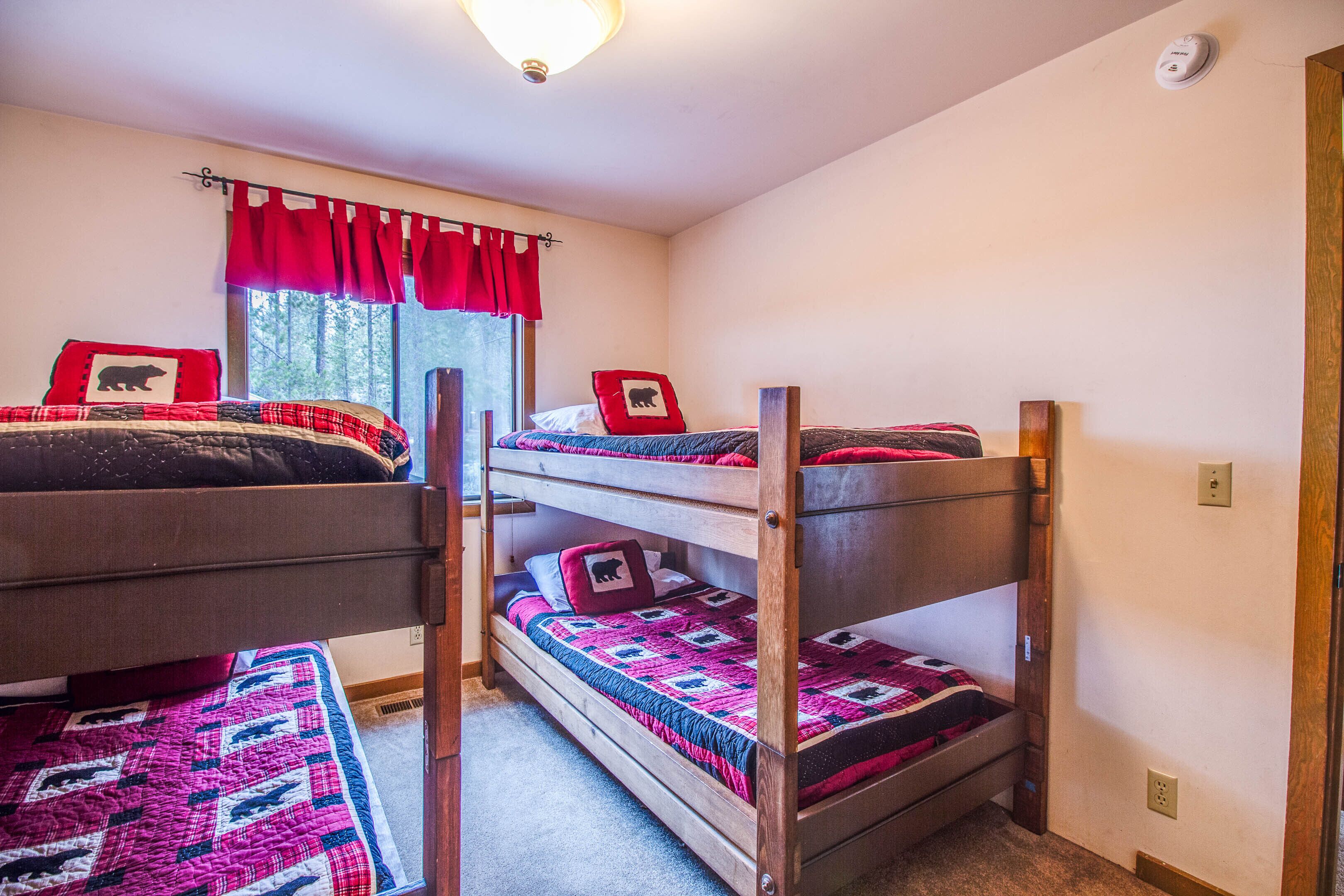 A bunk bed room with a window, red curtains, and a bear-themed pillow.