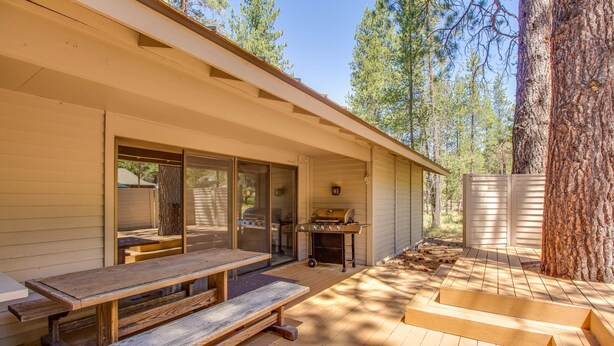 A wooden deck with a picnic table and grill area, surrounded by trees. - Cozy Pet Friendly Cabin, Wood Fireplace, Hot Tub, SHARC passes, close to Village (Sunriver)