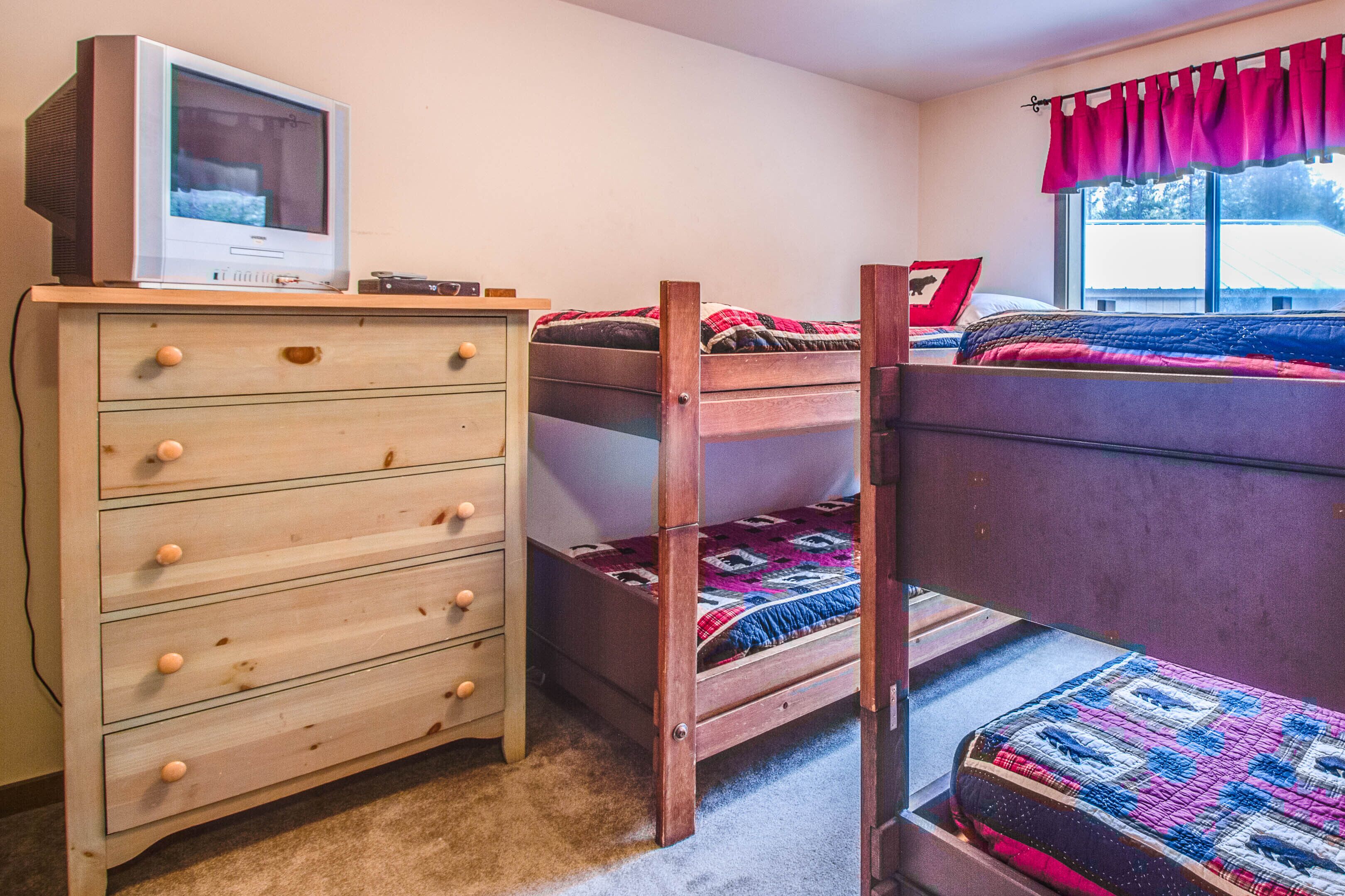 A bedroom with a wooden dresser, a bunk bed, and a window with curtains.