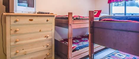 A bedroom with a wooden dresser, a bunk bed, and a window with curtains.