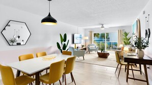 Een moderne woonkamer met een eethoek, met een witte tafel, gele stoelen en een groot raam met uitzicht op de omgeving.