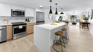 Een moderne keuken met witte kasten, roestvrijstalen apparatuur en een centraal eiland met barkrukken.