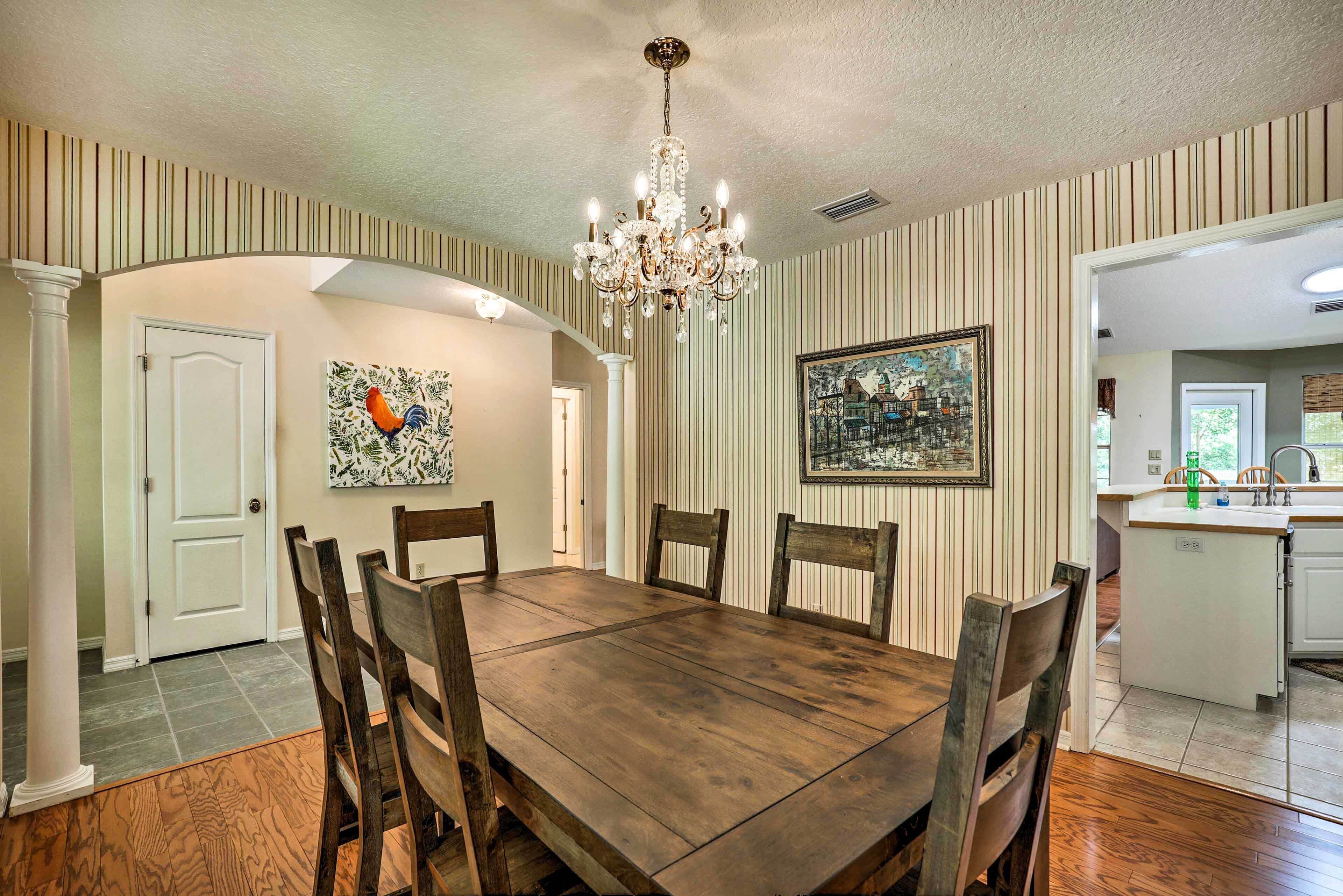 Une salle à manger avec une table et des chaises en bois, un lustre, un papier peint à rayures et un tableau au mur.