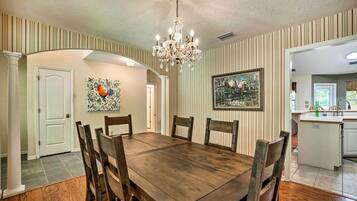 Une salle à manger avec une table et des chaises en bois, un lustre, un papier peint à rayures et un tableau au mur.