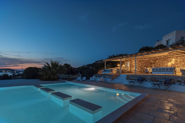 A swimming pool with steps leading into it, surrounded by outdoor seating and a stone wall.