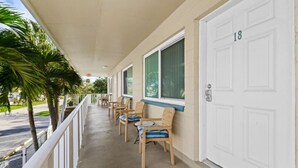 A motel with a covered porch, wooden chairs with blue cushions, and a white door marked with the number 18. - Beachy Madeira Getaway | Tropic Breeze Unit 18 – Steps to Beach, Pool Access (Madeira Beach)