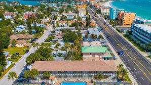 An aerial view of a coastal town with a prominent hotel featuring a swimming pool, a beachfront, and a busy road. - Beachy Madeira Getaway | Tropic Breeze Unit 18 – Steps to Beach, Pool Access (Madeira Beach)