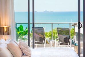 Ein Schlafzimmer mit Balkon und Meerblick, ein Bett mit Kissen, eine Lampe und zwei Sessel mit Polstern.