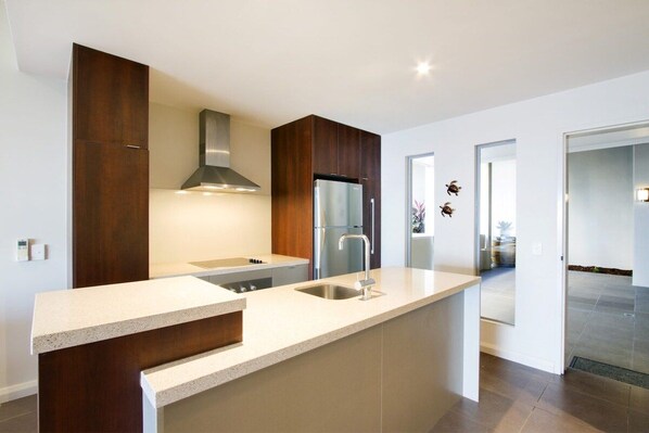 A modern kitchen with a central island, stainless steel appliances, and dark wood cabinetry. - Oscar's View - Airlie Beach (Airlie Beach)