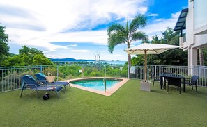 A backyard with a swimming pool, lounge chairs, a table, and a dining area. - Oscar's View - Airlie Beach (Airlie Beach)