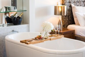 Ein Badezimmer mit einer Badewanne, einem Holztablett, einer Blumenvase und einer Champagnerflasche.