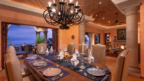 A dining area with a long table set for a meal, surrounded by chairs, with a chandelier above. - Spacious Open-Air Villa w/Unequaled Luxury/Views, 5 Mins to Town, Chef & Staff (Puerto Vallarta)