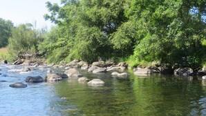 A river with clear water, surrounded by rocks and dense green foliage.