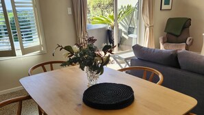 Een eethoek met een houten tafel, vier stoelen, een vaas met bloemen en uitzicht op een tuin door een glazen schuifdeur.