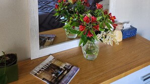 A bedroom with a bed, a nightstand, a mirror, and a vase with flowers.