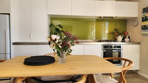 Een moderne keuken met witte kastjes, een groene spatwand en een houten eettafel met stoelen.