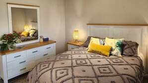Een slaapkamer met een bed, een kaptafel, een spiegel en een nachtkastje met een lamp.