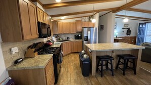 A kitchen with wooden cabinets, a stainless steel refrigerator, a microwave, and a gas stove. There are two stools at the island, and a trash can is visible. - Best of both worlds! Amazing views plus an easy walk into town! (New Paltz)