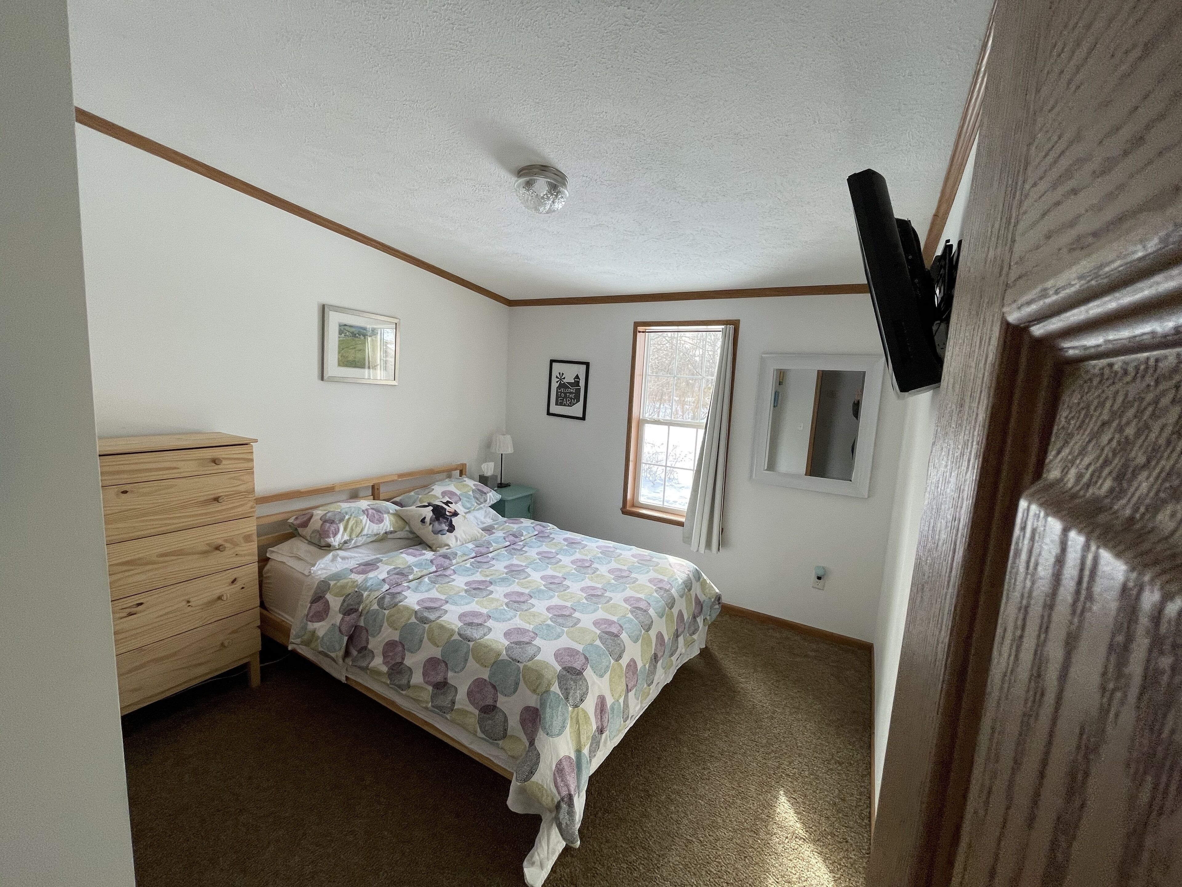 A bedroom with a bed, wooden dresser, and a window.