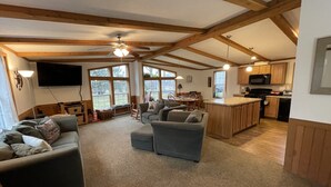 A spacious living area with a large grey sofa, a wooden ceiling, and a kitchen area with wooden cabinets and a black microwave. - Best of both worlds! Amazing views plus an easy walk into town! (New Paltz)