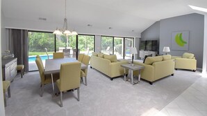 Un salon spacieux comprenant un coin repas, de grandes fenêtres et une vue sur une piscine.