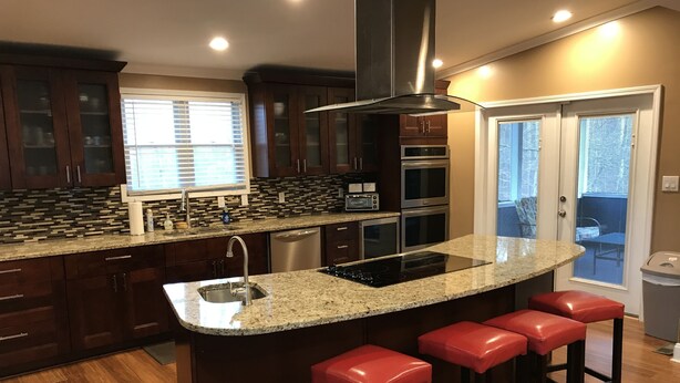 Una cocina moderna con armarios de madera oscura, encimera de granito, electrodomésticos de acero inoxidable y una zona con taburetes de bar.