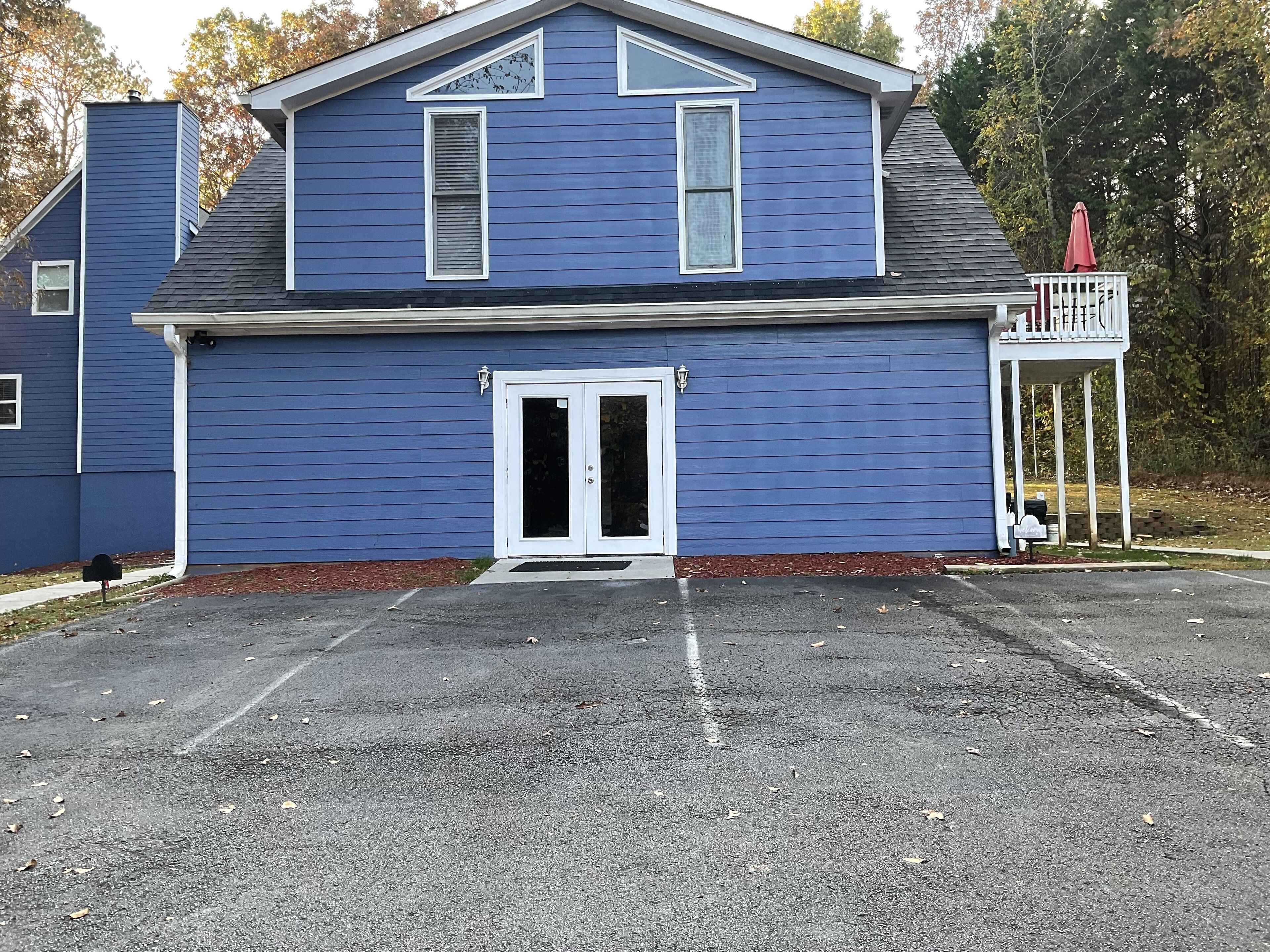 A two-story building with a blue exterior, a front door, and a small porch with a red umbrella.