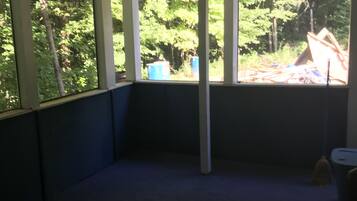 A room with a ceiling fan, large windows, and a view of trees and outdoor debris.