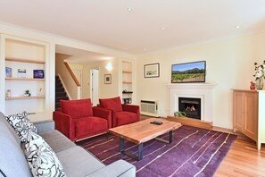 A living room with a red sofa, a grey sofa, a wooden coffee table, a fireplace, and a television mounted on the wall.