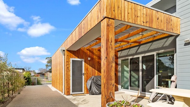 A modern wooden building with a covered patio area, large sliding glass doors, and a visible outdoor seating area.