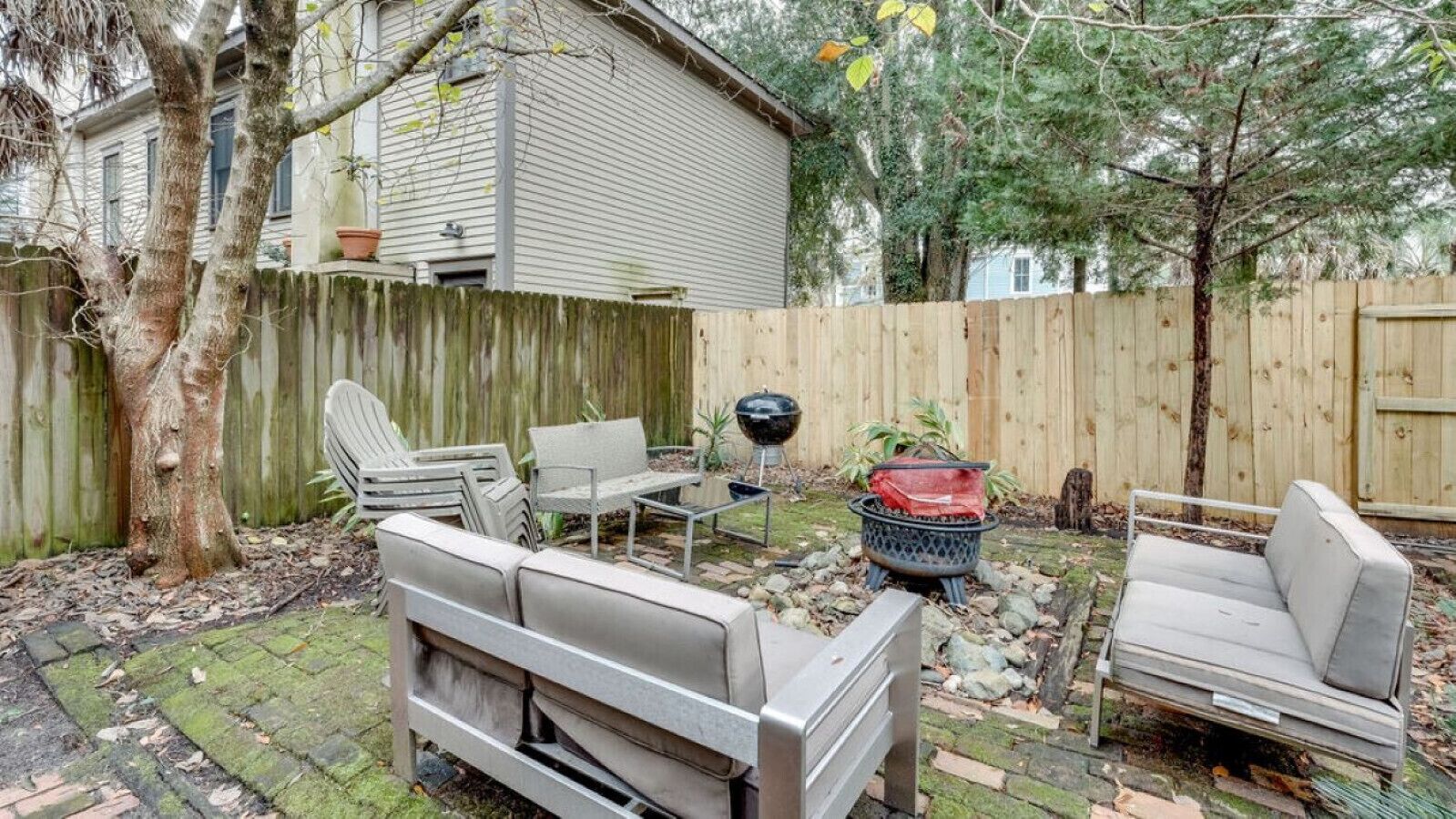 Un jardin avec une terrasse en bois, un barbecue et du mobilier d’extérieur comprenant un canapé et des fauteuils.