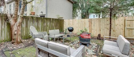 Un jardin avec une terrasse en bois, un barbecue et du mobilier d’extérieur comprenant un canapé et des fauteuils.