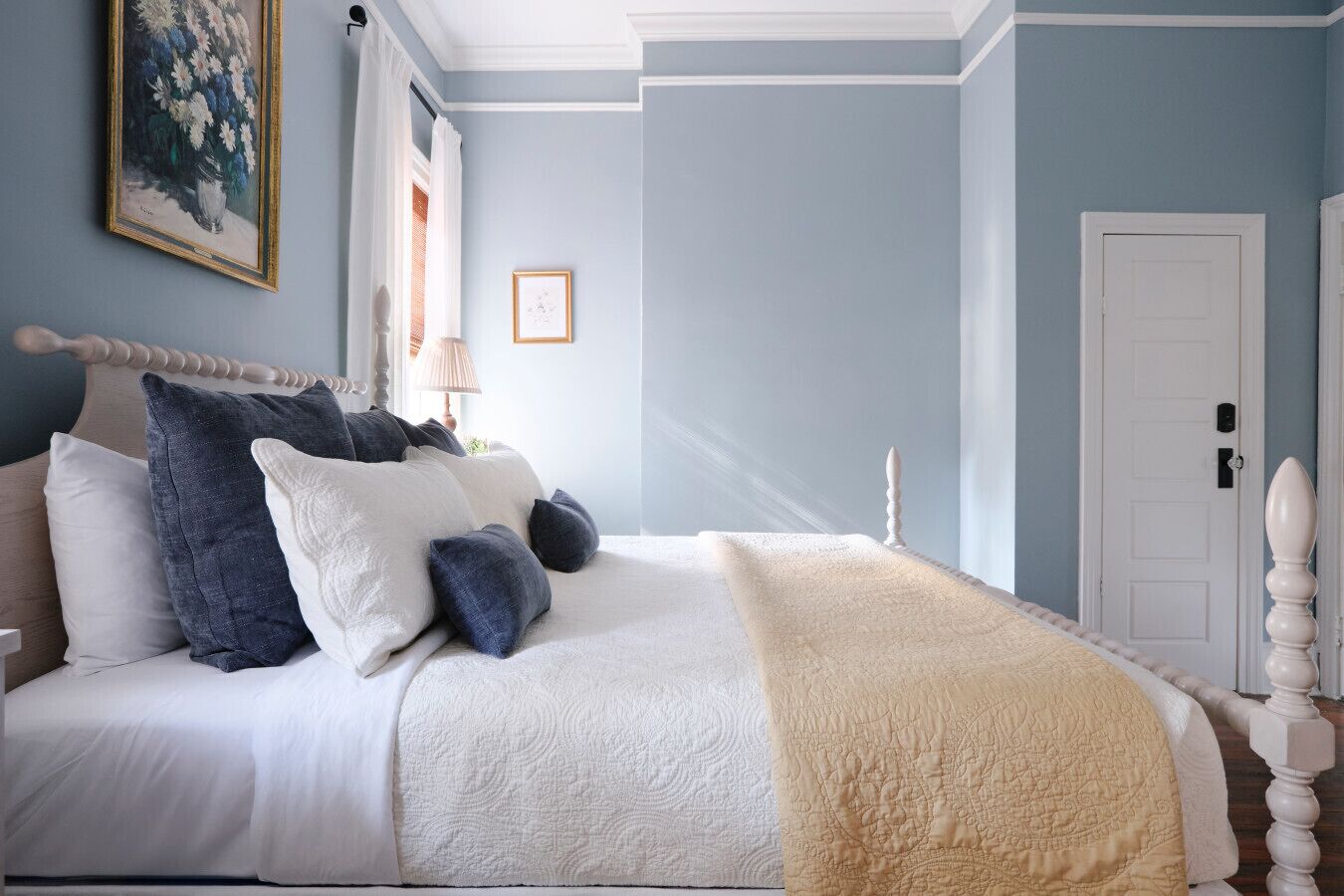 Une chambre à coucher avec un lit, des oreillers, une table de chevet, une lampe, un tableau encadré et une porte.