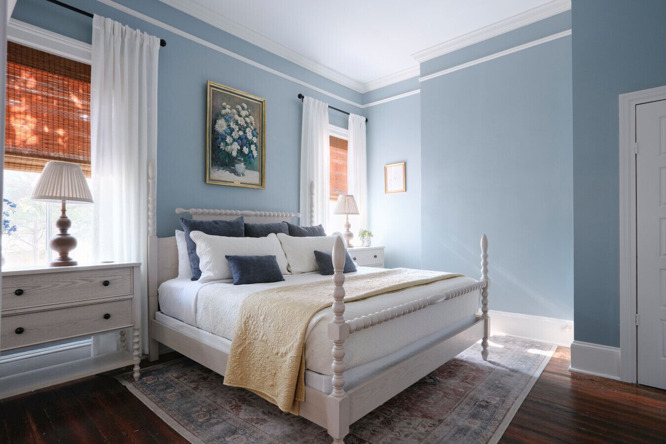 A bedroom with a four-poster bed, a nightstand, a dresser, and a window with curtains.
