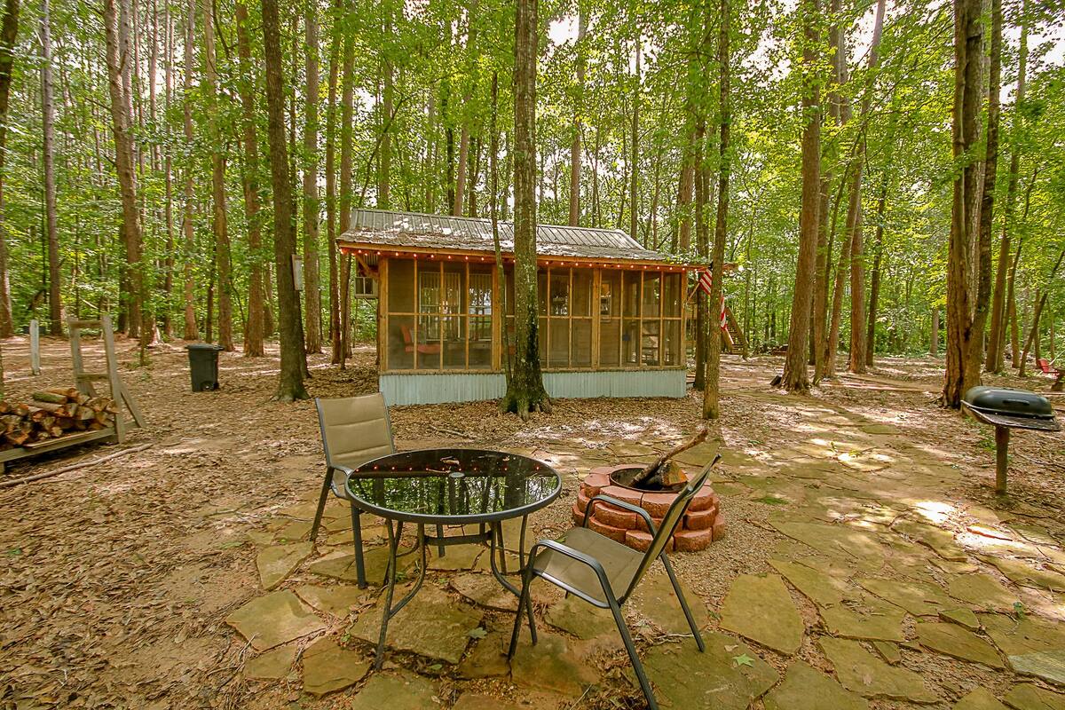 Una cabaña rústica con un patio de piedra, una fogata y una mesa de comedor con sillas.