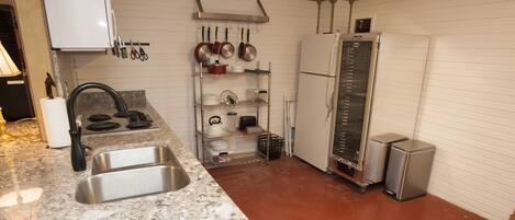 Una cocina con encimera de granito, pileta de acero inoxidable, alacenas blancas y piso rojo.