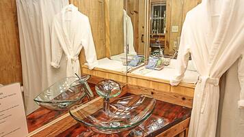 A bathroom with wooden walls, a large mirror, and a vanity with a glass bowl centerpiece.