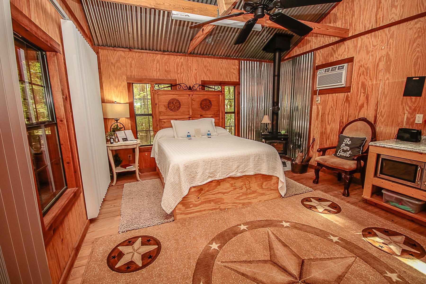 A cozy wooden bedroom with a large bed, a desk with a chair, a ceiling fan, and a fireplace.