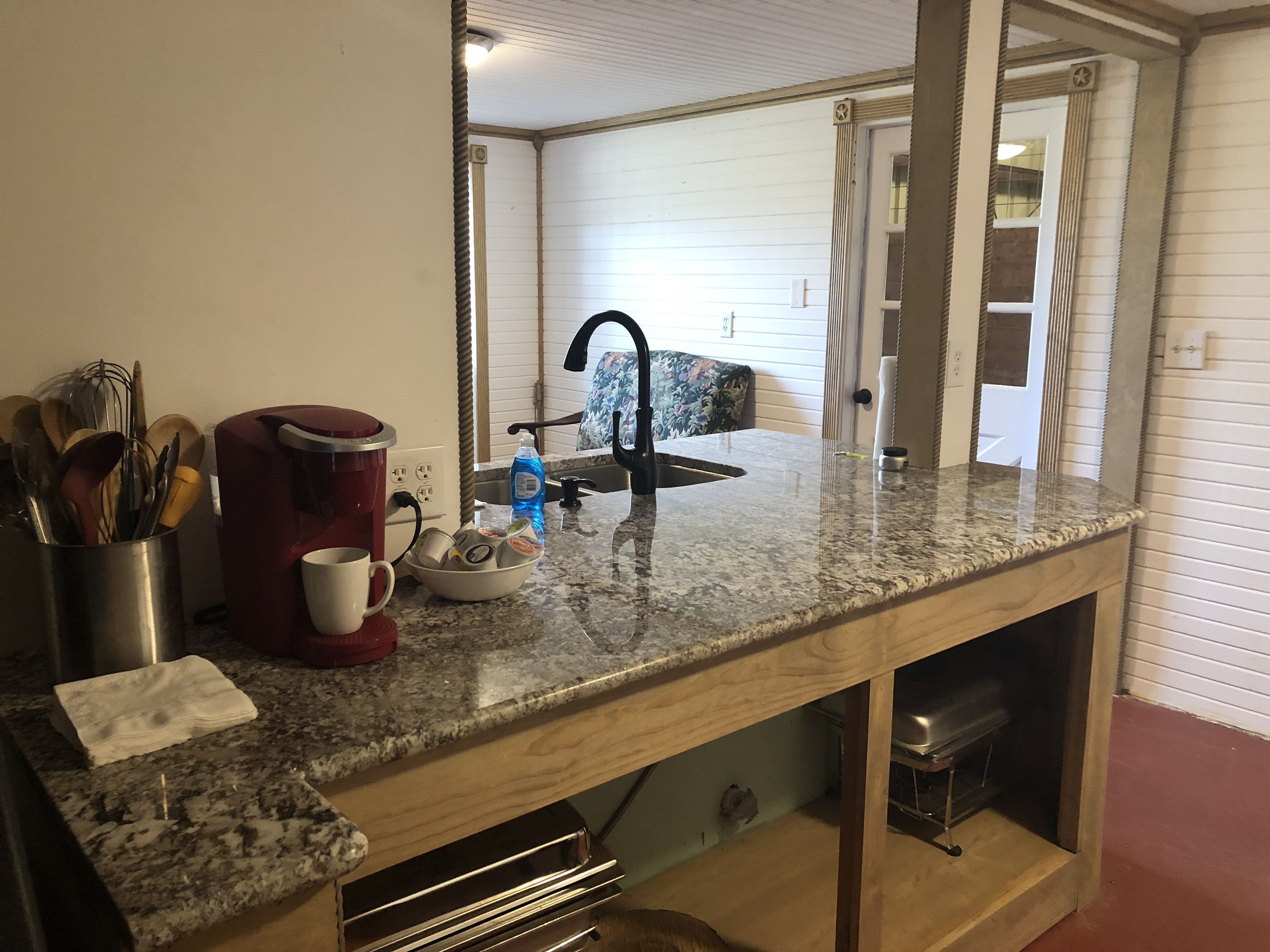 Una cocina con encimera de granito, una cafetera roja, un lavabo y un espejo que refleja la habitación.