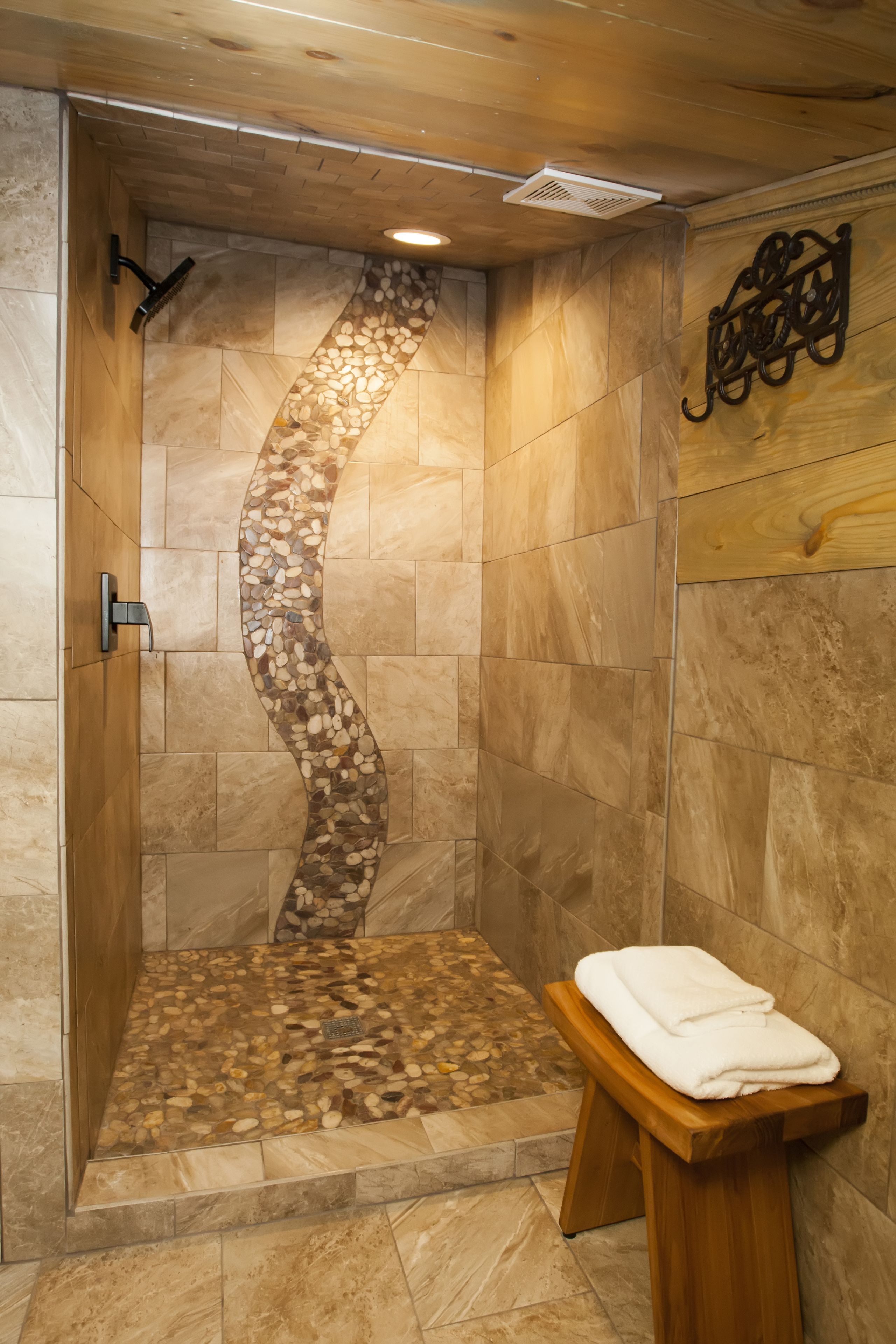 Ducha con diseño de mosaico curvo, banca de madera con toalla y lámpara de pared.