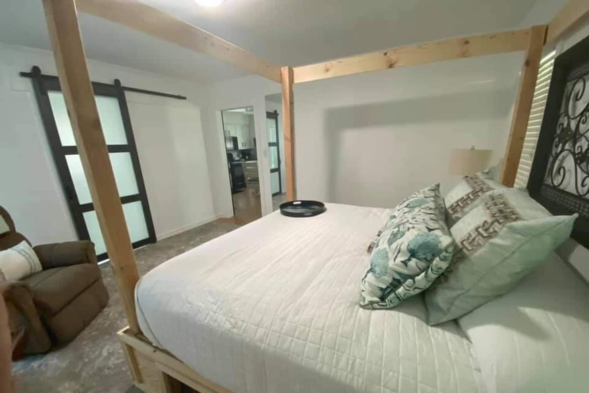 Un dormitorio con estructura de cama de madera, un sofá y una cocina al fondo.