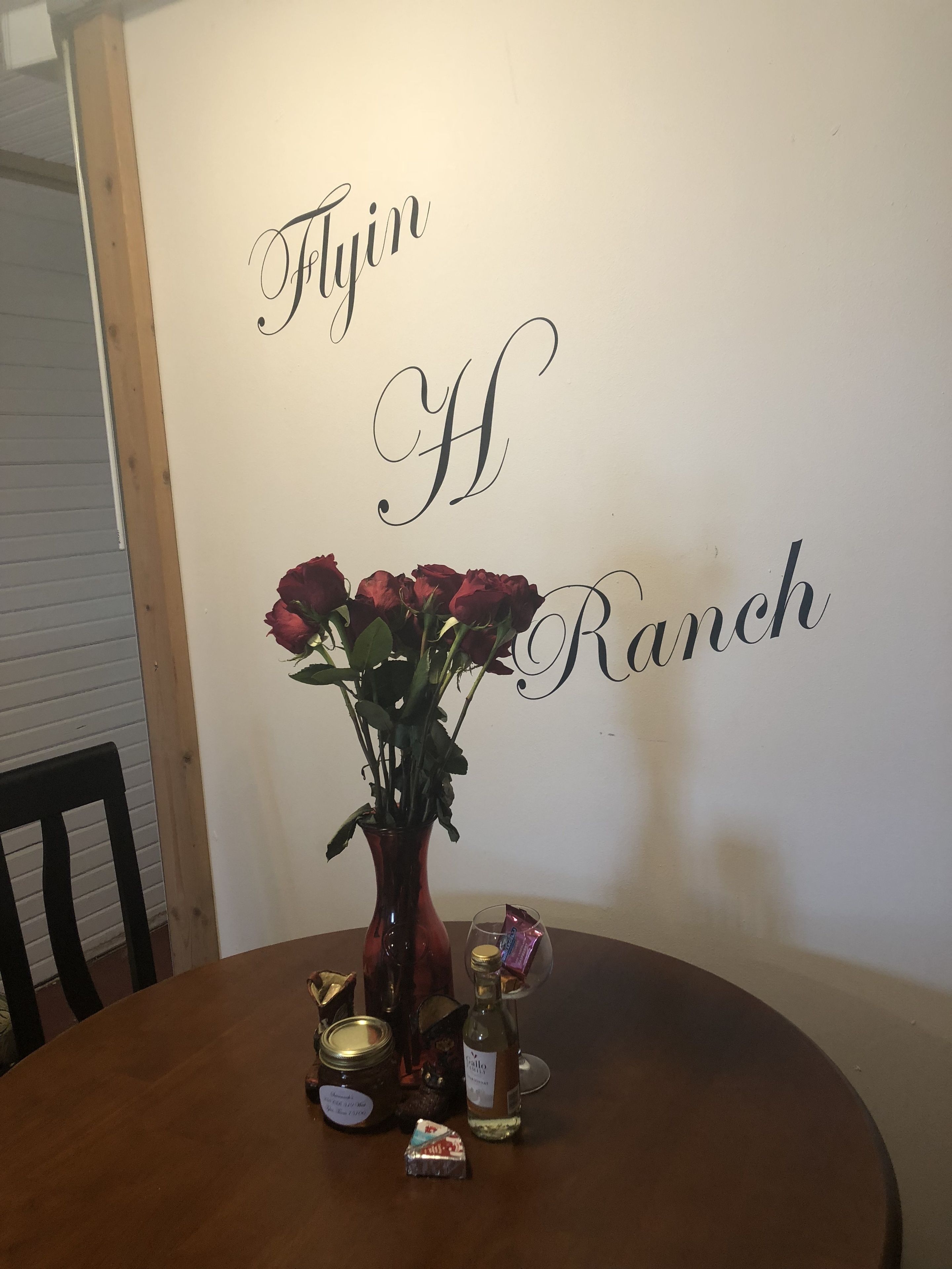 A dining table with a vase of red roses, a bottle of wine, and some food items.