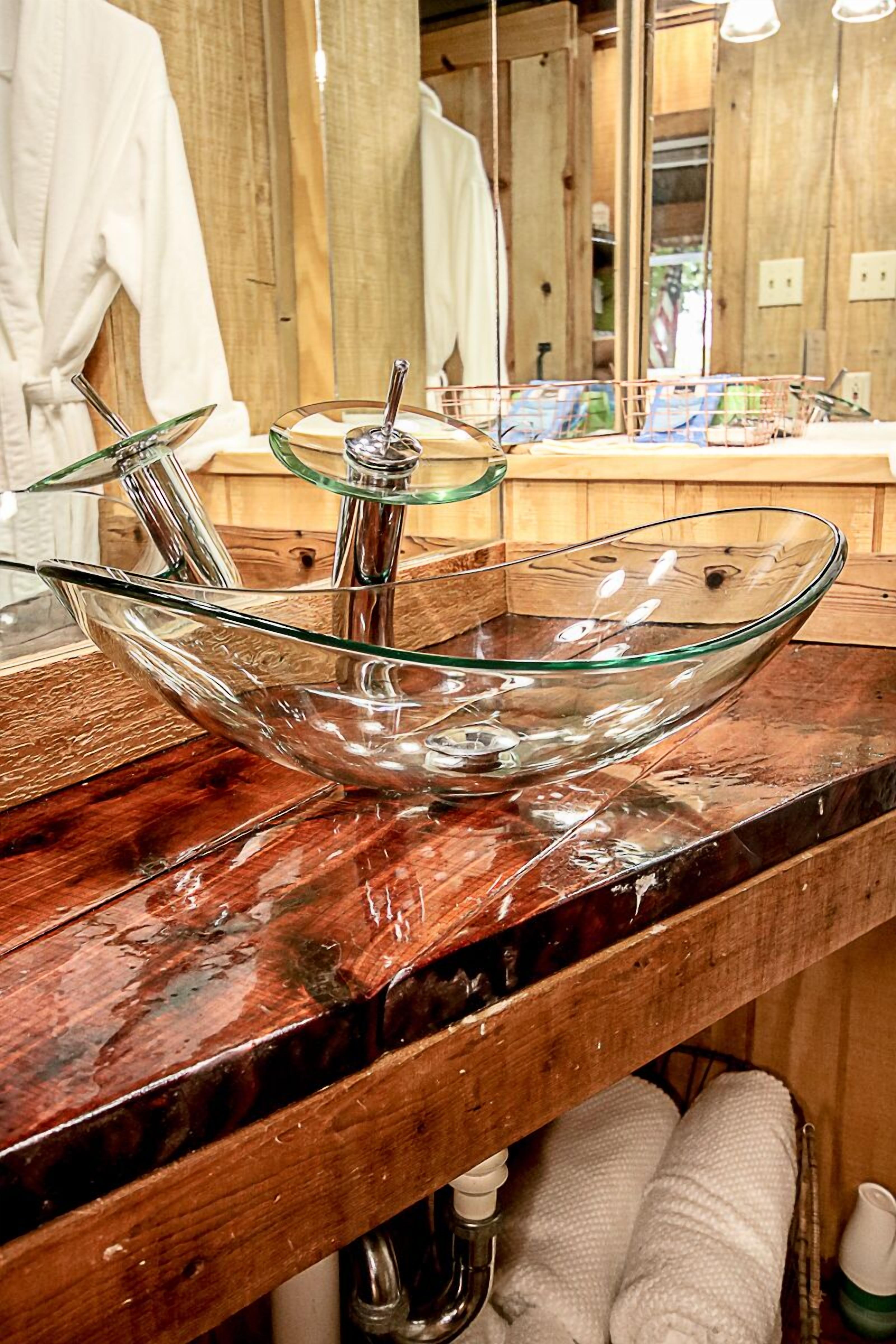 A glass bowl sink with a faucet on a wooden countertop in a bathroom.