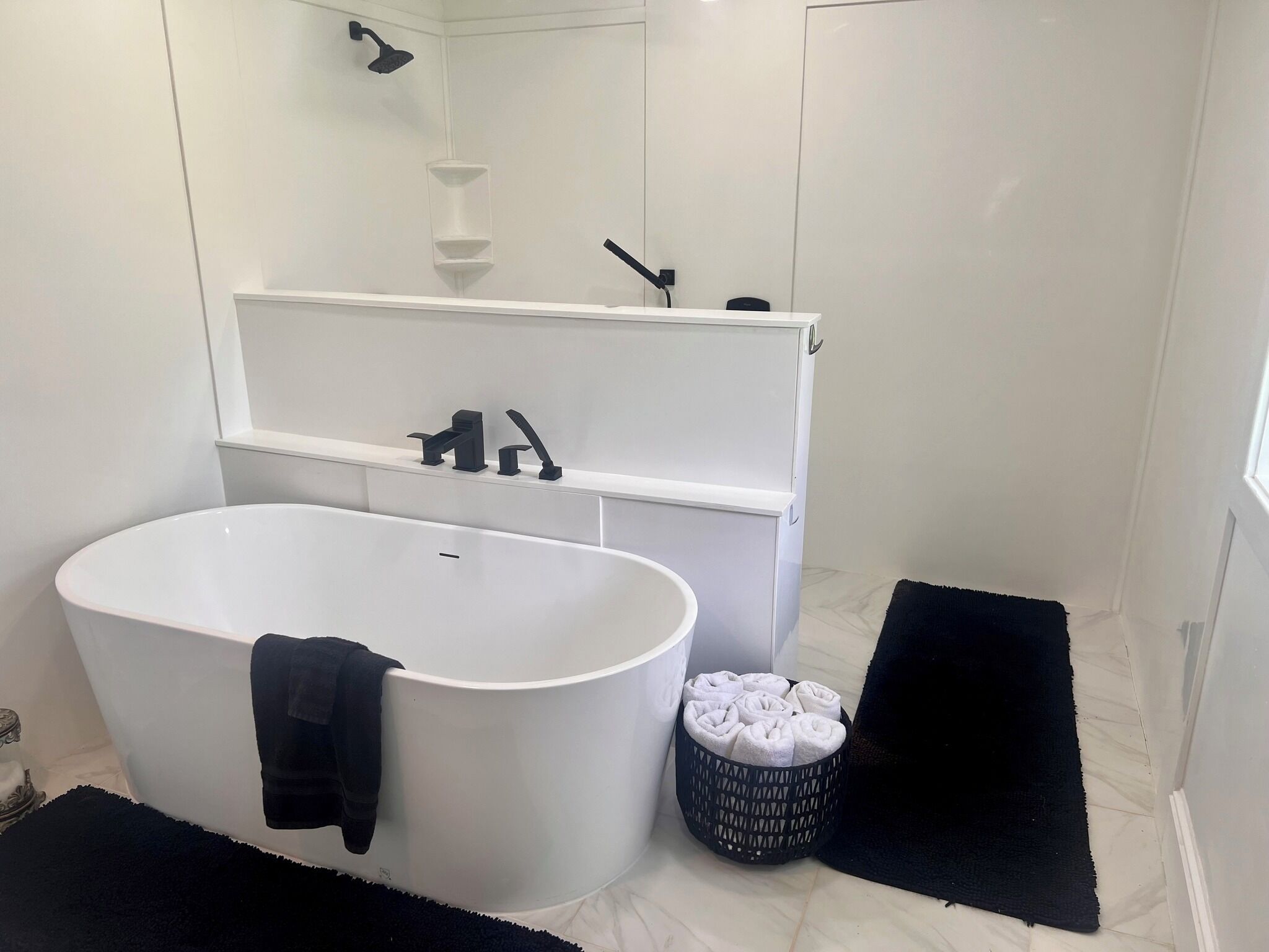 A modern bathroom with a freestanding bathtub, a white vanity with a mirror, and a black bath mat.