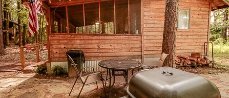A rustic cabin with a covered patio, a grill, and a flag.