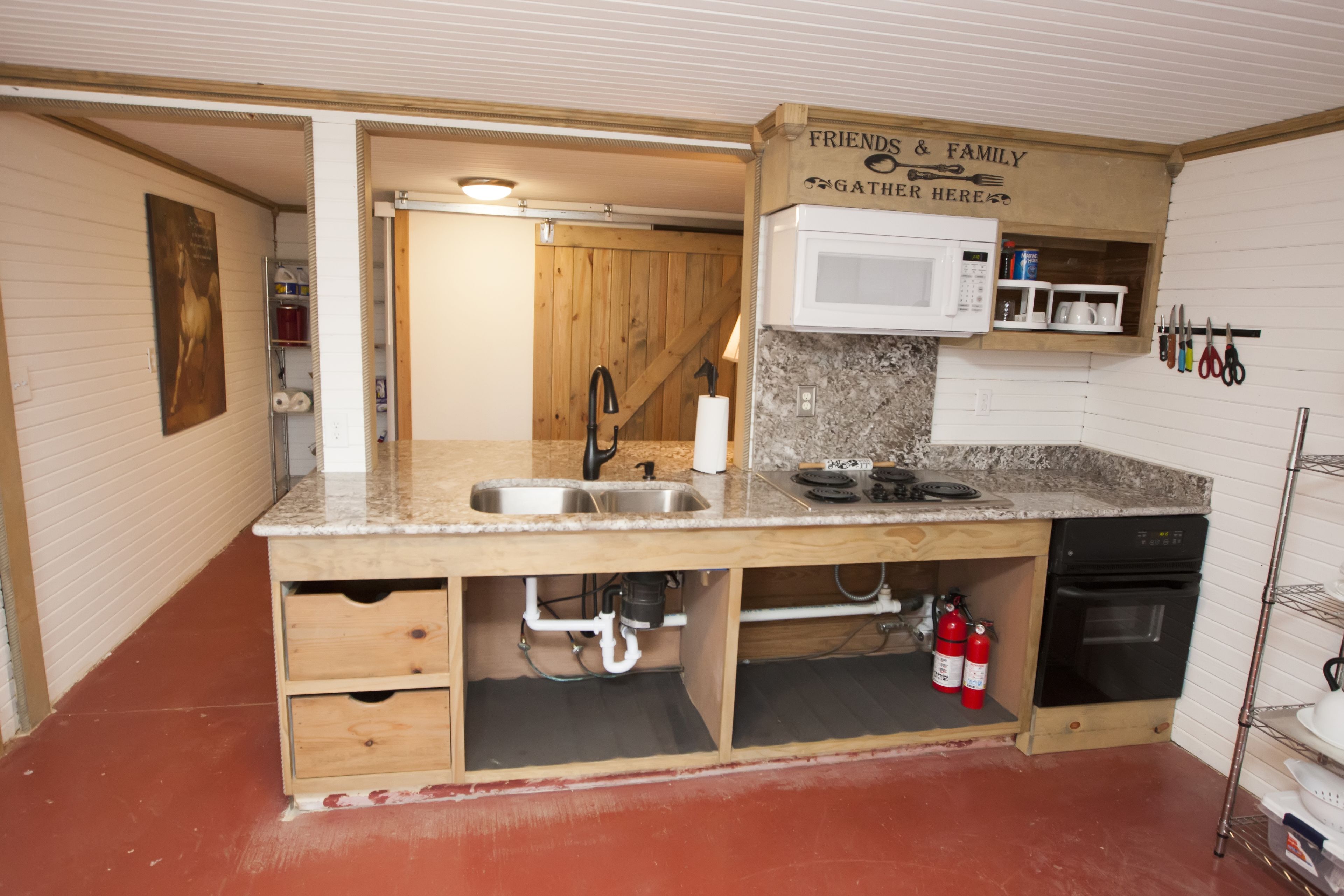 A compact kitchen with a built-in microwave, sink, and stove. There is a wooden cabinet with a 'Friends & Family Gather Here' sign.