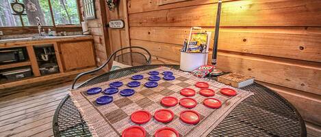 L’intérieur d’un chalet en bois, avec une table ronde dressée pour un jeu, une lampe et une enseigne indiquant « The Porch ».