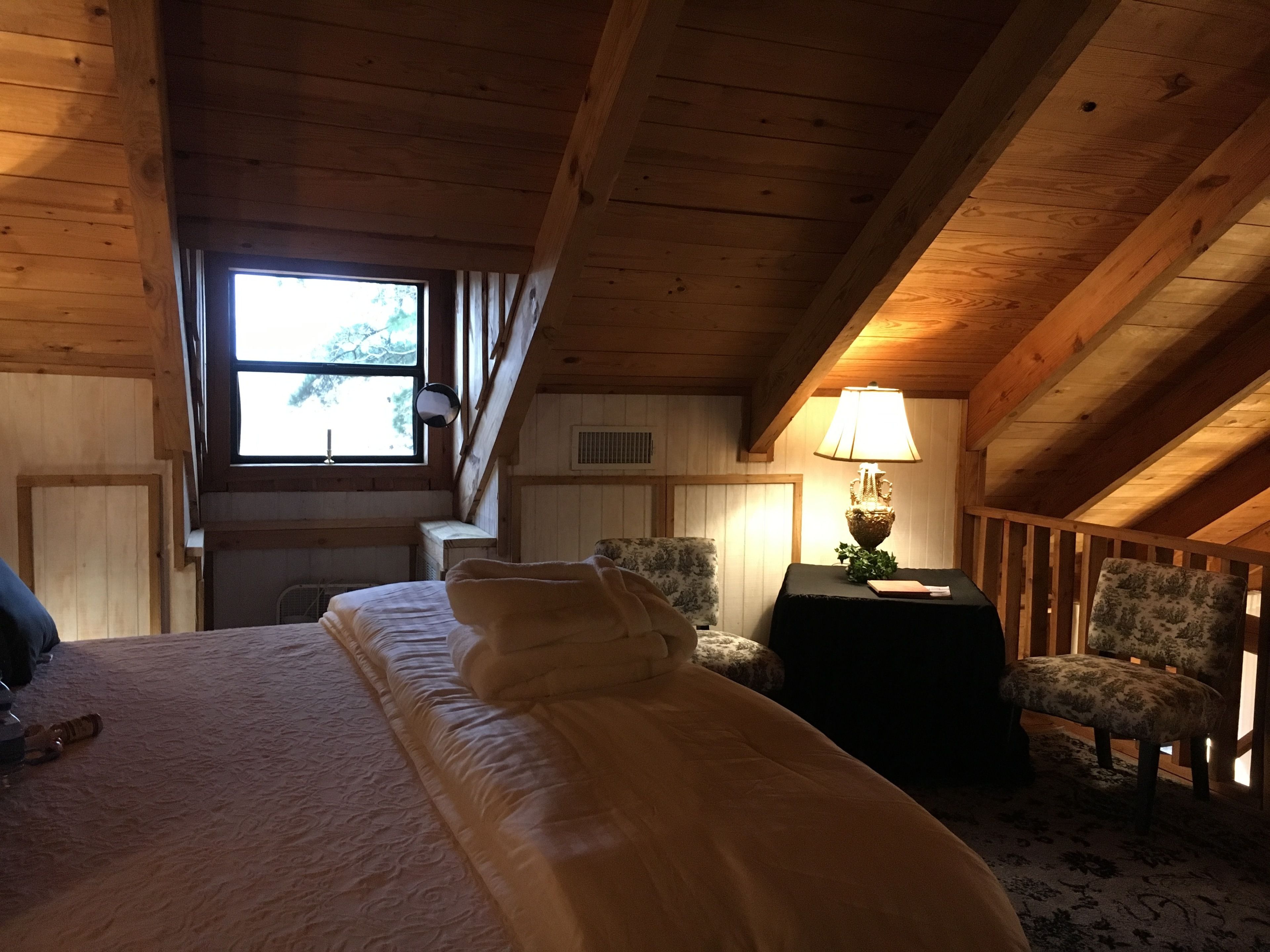 A cozy attic bedroom with a bed, a chair, a lamp, and a window.